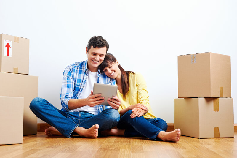 Apartment hunting. Couple looking at tablet while moving into new home with boxes