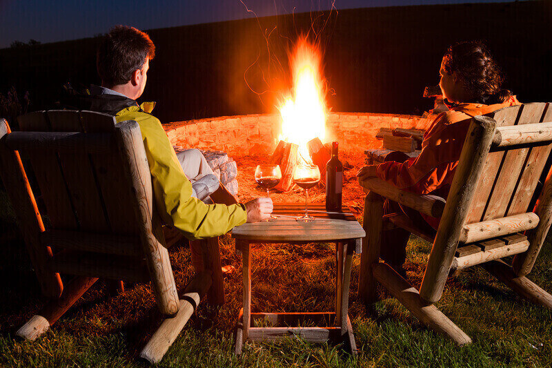 A couple is sitting by the bonfire, enjoying wine